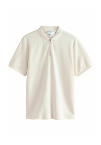 Camisa polo en beige claro con mangas cortas, de textura suave y con cremallera hasta un cuarto. Presenta un sutil patrón de canalé en el cuerpo.