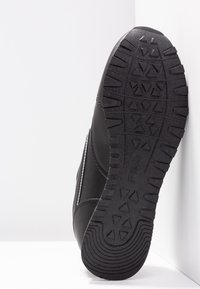 Scarpa sportiva nera con suola in gomma testurizzata, tomaia sintetica liscia, cuciture a contrasto e punta arrotondata.