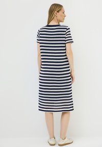 Gestreiftes Kleid in Marineblau und Weiß, mit kurzen Ärmeln und lockerem Schnitt. Hergestellt aus strukturierter Stoff, knielang mit seitlichen Schlitzen.