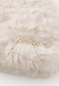 Soft beige faux fur fabric with a small gold metallic "Guess" logo embedded on the surface.