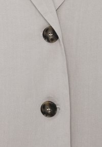 Deux boutons brun foncé sur un tissu gris clair, montrant un bord plié près du bouton supérieur.