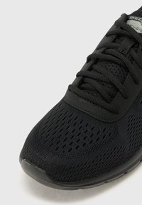 Black athletic shoe featuring a mesh upper with perforations, flat laces, and a cushioned sole, designed for breathability and comfort.
