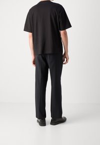 Czarny bawełniany t-shirt z krótkim rękawem o luźnym kroju, w zestawieniu z dopasowanymi czarnymi spodniami oraz czarnymi butami na jednolitym tle.