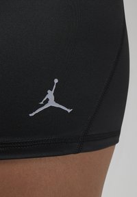 Crne atletske šortse napravljene od rastezljivog materijala s glatkom teksturom, s bijelim Jumpman logotipom i kontrastnim detaljima šivanja.