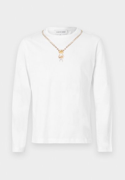 Fehér, hosszú ujjú pamut póló, aranyszínű lánc nyaklánccal, medál részletekkel és laza szabással.