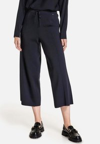 Svarta, vida byxor i mjukt tyg med elastisk dragsko i midjan. Har vertikala sömmar och cropped längd. Matchas med svarta loafers.