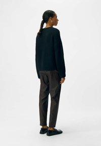 Zwarte oversized trui met een textuur, gecombineerd met donkerbruine tapse broek en zwarte schoenen, gezien vanuit de rug.