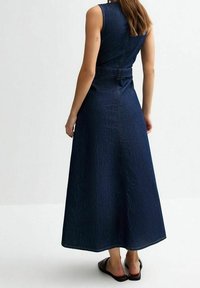 Jeansmaxiklänning, mörkblå, ärmlös, figurnära liv, åtsittande midja med snörning, utsvängd kjol, mjuk textur, minimalistisk design.