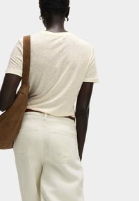Camicia beige a maniche corte con una sottile trama, abbinata a pantaloni larghi beige chiaro e una borsa a tracolla marrone. Vista da dietro, design minimalista.