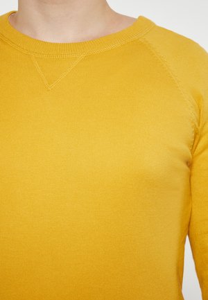 Keltainen raidoitettu neulepusero, jossa on pyöreä pääntie ja raglan-hihat. Puserossa on sileä pinta ja siistit saumat.