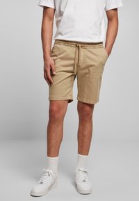 Shorts beige fino al ginocchio in cotone con cintura elastica e stringa da raccogliere. Indossati con sneakers bianche e calze. Design semplice.