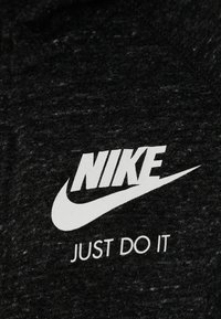 Nike-logotypen och swoosh med sloganen "Just Do It" tryckt i vitt på mörkgrå texturerad tyg.