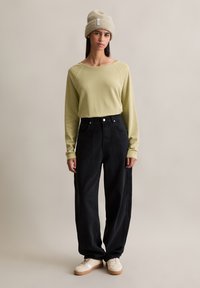 Jasnozielona koszula z długim rękawem, czarne spodnie typu wide-leg i beżowe sneakersy. Modelka nosi beżową dzianinową czapkę. Prosty, casualowy styl.
