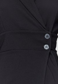 Černé sakové šaty s překládaným designem, hladkou texturou a dvěma dekoračními šedými knoflíky na pase.