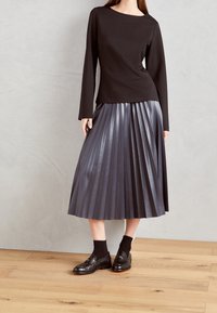 Haut noir à manches longues avec un col rond, associé à une jupe midi plissée gris foncé. Des chaussettes noires et des chaussures complètent la tenue.