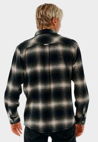 Camisa de franela de cuadros en blanco y negro con mangas largas, puños abotonados, dobladillo redondeado y detalle de pinzas en la parte trasera.