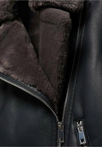 Veste en cuir noire avec une douce doublure en fourrure brun foncé, deux zips en argent et un cuir texturé pour un détail supplémentaire.
