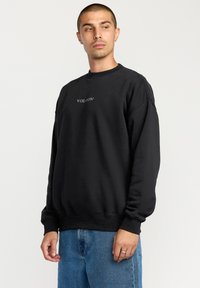 Black sweatshirt with a crew neckline, featuring a small "VOLCOM" logo in white. Made of soft fabric, with ribbed cuffs and hem.