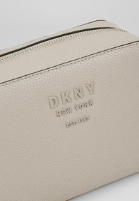 Pochette in pelle beige testurizzata con cerniera argentata e logo DKNY New York EST. 1989 impresso in rilievo sul davanti.