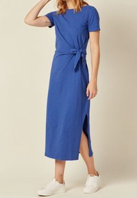 Vestido azul de largo a la rodilla con mangas cortas, detalle de cintura atada y abertura lateral. Combinado con zapatillas blancas, con una tela suave y texturada.