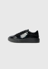Sapatilhas pretas de couro envernizado com bico arredondado, sola de borracha plana e atacadores pretos. Apresenta um design minimalista e uma textura elegante.