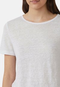 T-shirt blanc à manches courtes en coton léger avec une texture douce et un col rond classique ; coupe décontractée au niveau de la poitrine.