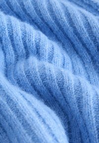 Soft, light blue knitted fabric with a ribbed pattern and fuzzy texture in close-up detail.
