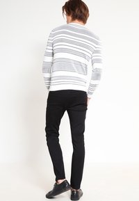 Suéter a rayas blancas y grises, pantalones negros y zapatos negros. El suéter presenta rayas horizontales y un dobladillo canalé. Diseñado para un ajuste casual.