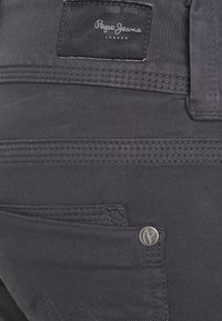 Ciemnoszare dżinsy z przeszywaną kieszenią i metalowym guzikiem z logo. W pasie znajduje się etykieta z tkaniny z napisem "Pepe Jeans London."