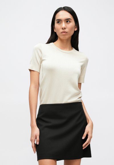 Chemisier beige à manches courtes en tissu lisse associé à une jupe noire ajustée. Les deux vêtements présentent des lignes épurées et un design simple.