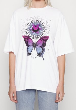 Hvid oversized T-shirt med lilla og blå sommerfugl under et stiliseret sol- og månegrafik, båret med lyseblå jeans.