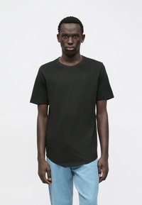 Černé bavlněné tričko s kulatým výstřihem, volným střihem, krátkými rukávy a rovnýlem lemováním. Nošeno s světle modrými džínami.