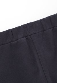 Pantalon en mélange coton gris foncé avec une taille élastique et une texture douce. Il présente un design simple sans matériel visible ni motifs.