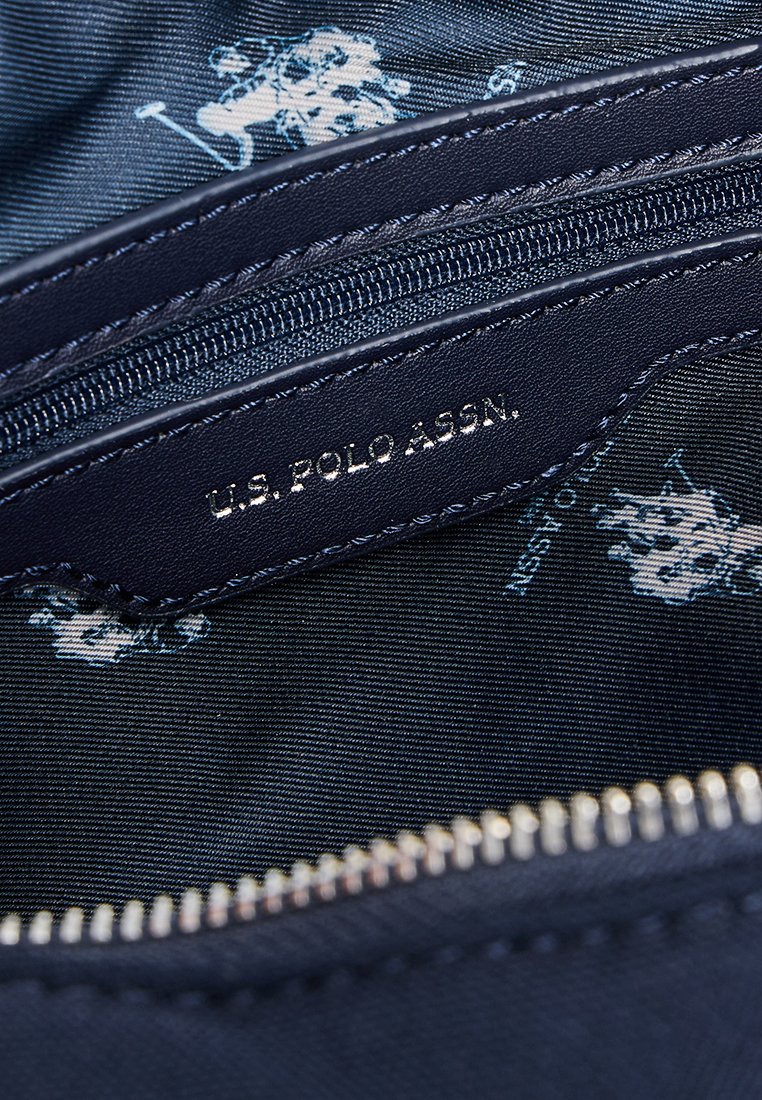 Granatowa tkanina wewnętrzna z logo U.S. Polo Assn. Posiada srebrny zamek błyskawiczny oraz wzorowane podszewkę z subtelnymi motywami gracza polo.