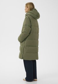 Oliven grøn pufferjakke med hætte, der har vandrette kviltede sektioner, sidelommer og et knælangt design.