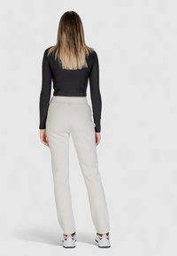 Top aderente nero a maniche lunghe abbinato a pantaloni crema, caratterizzati da una superficie liscia e un alto punto vita, completati da scarpe da ginnastica.