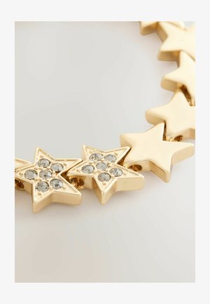 Zlato obarvana ogrlica, ki vsebuje povezane oblike zvezd, nekatere okrašene s prozornimi rhinestones za dodatno podrobnost in teksturo.