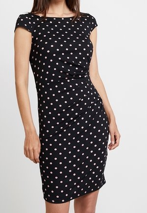 Schwarzes eng anliegendes Kleid mit pinkfarbenen Punkten, kurzen Kappenärmeln und gerafftem Detail an der Taille, getragen von einer stehenden Frau.