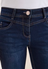 Granatowe dżinsy wykonane z denimu, o dopasowanym kroju, pięciopocketowej stylizacji, z kontrastowym szwem i zapięciem na guzik w talii.