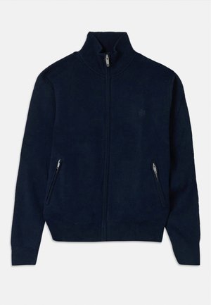 Sudadera navy con cremallera y cuello alto, con dos bolsillos laterales con cremallera y una tela de textura suave. Presenta un logo sutil en el pecho.