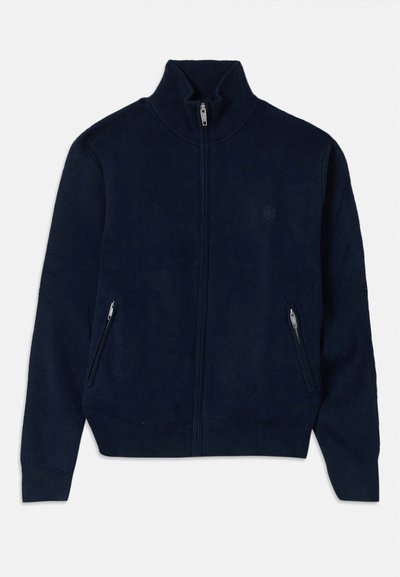 Sudadera navy con cremallera y cuello alto, con dos bolsillos laterales con cremallera y una tela de textura suave. Presenta un logo sutil en el pecho.