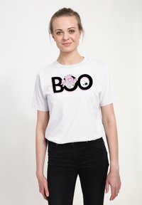 Bílý bavlněný tričko s grafikou "BOO" v tučném černém písmu a růžovou postavičkou, předváděno na modelu v černých džínách.