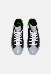 Zapatillas altas negras y grises con cordones blancos, detalles verdes y suelas de goma transparentes. Se pueden ver materiales lisos y texturizados.