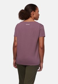 T-shirt a maniche corte e collo rotondo in tessuto viola chiaro. Presenta una texture liscia con un logo bianco a contrasto sul retro del collo.