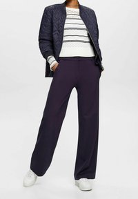 Veste bomber matelassée bleu marine, pull blanc à rayures bleu marine, et pantalon large violet foncé. Des baskets blanches complètent la tenue.