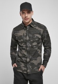 Camo-mønstret skjorte i nuancer af grøn og grå, med knaplukning, to forlommer og spids krave.