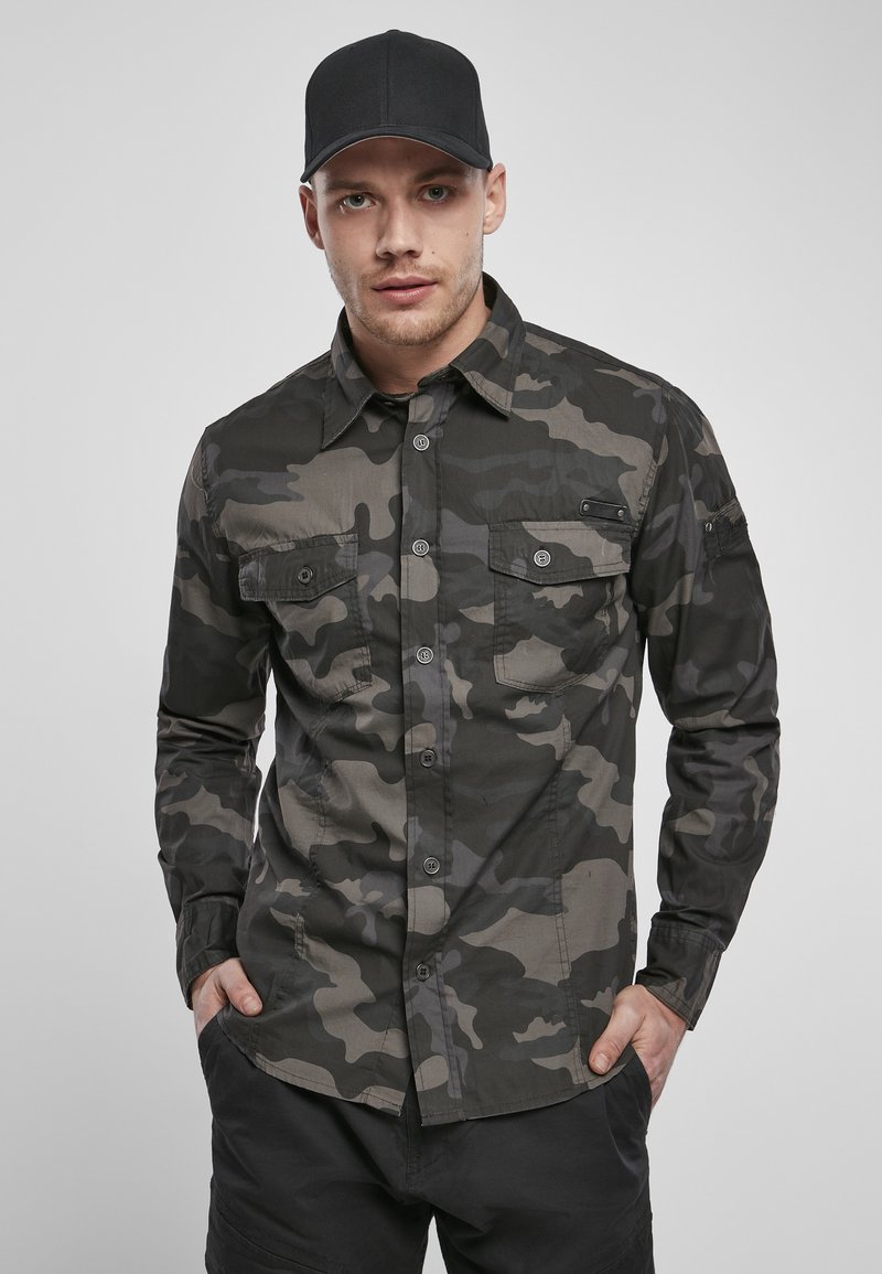 Camo-patterned shirt in shades of green and gray, featuring a button-up design, two front pockets, and a pointed collar.