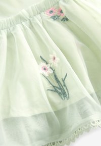 Vihreä tylli kangas, jossa on kukkakirjonta, jossa on vaaleanpunaisia ja valkoisia päivänkakkaroita, kerätty vyötärö ja pitsireuna helmassa.