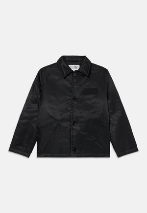 Casaco de cetim preto com colarinho pontudo, fecho frontal com botão, dois bolsos laterais e um emblema texturizado no peito.