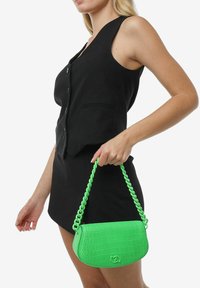 Grøn faux krokodille crossover taske med en kraftig kædestrop, der har en rund form og præget logo på forsiden.